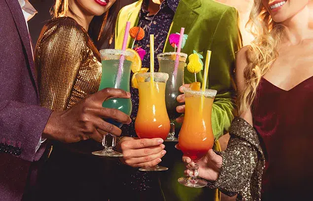 Invitados elegantes sosteniendo cócteles tropicales coloridos, servicio de coctelería y experiencias corporativas.