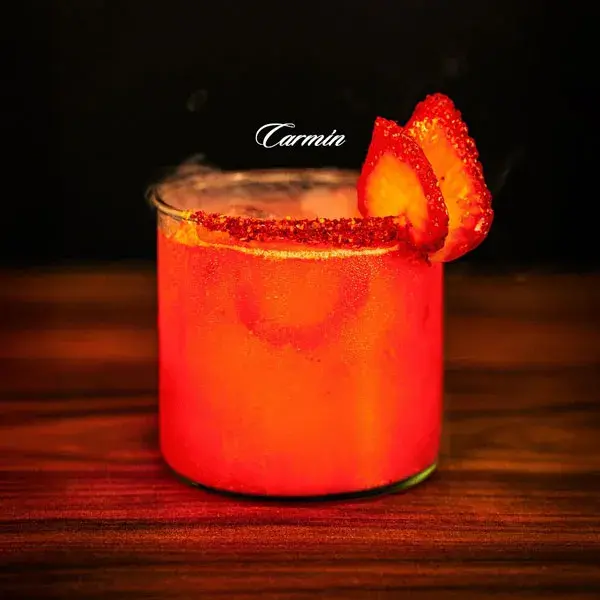 Cóctel de autor de color carmín con hielo y rodaja de limón, una creación premium de mixología artística.
