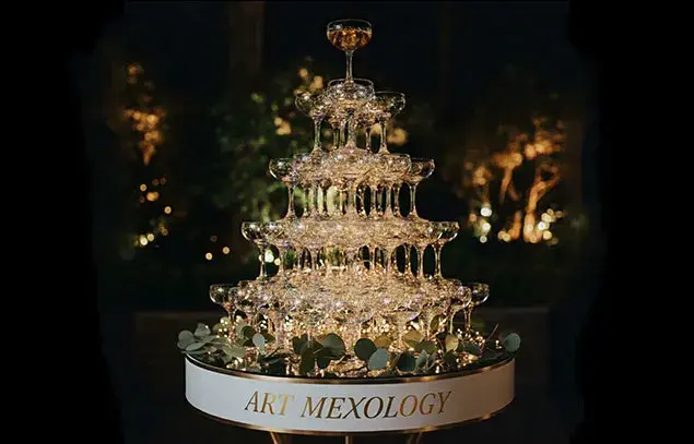 Torre de copas de champaña iluminada con letrero de Art Mexology, servicio exclusivo de mixología para bodas.