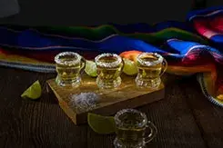 Shots de tequila artesanal escarchados con sal, limones y textil colorido mexicano, una muestra de coctelería tradicional.
