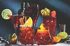 Variedad de cócteles de autor color rojo con rodajas de naranja, limón y canela, una experiencia premium de mixología artística.