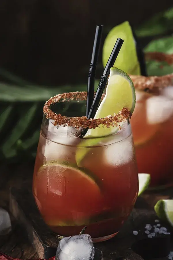 Cóctel refrescante con hielo y rodajas de limón, escarchado con sal de gusano o chile para una experiencia de mixología artística.